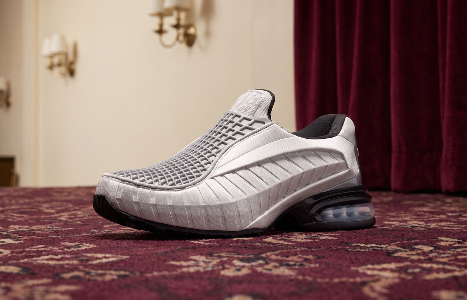 Nike Air Max Dolce Metallic Silver met veterloze kooi-upper en zichtbare Air op bordeaux tapijt in een bioscoopfoyer