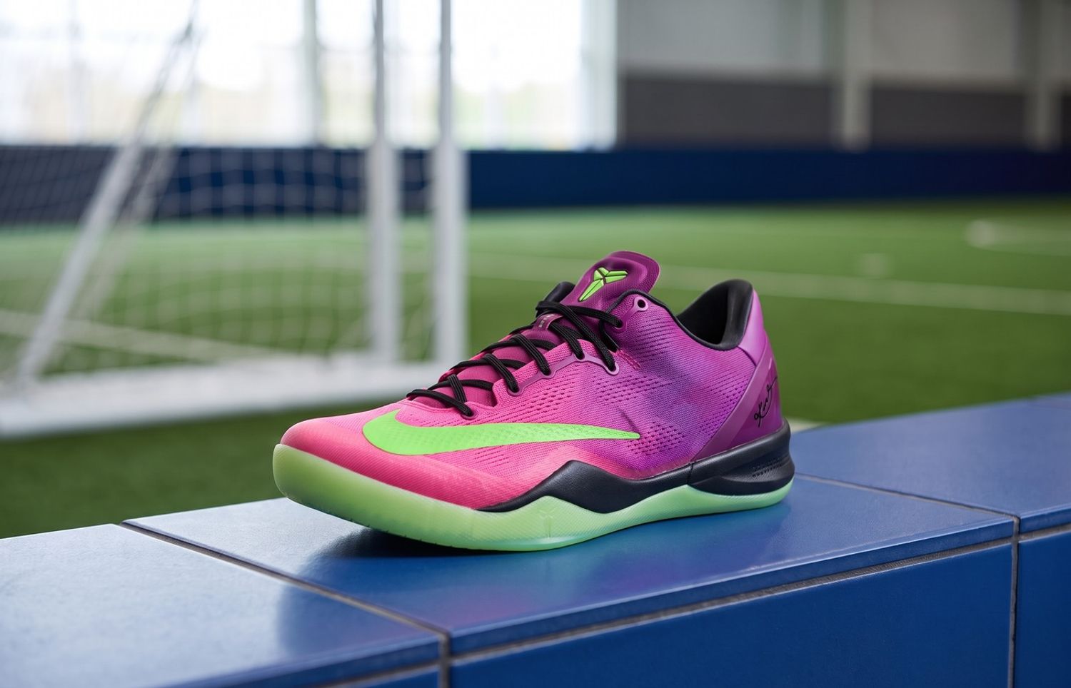 Nike Kobe 8 Protro Mambacurial met roze-paars mesh en groene zool op een blauwe tegelbank bij een voetbalveld