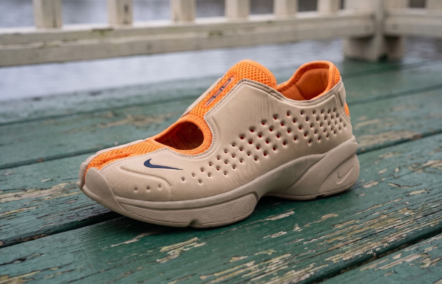 Nike Rift 2 Vivid Orange/Yukon Tan met oranje mesh, geperforeerde bruine upper en gespleten neus op een groene houten roeisteiger