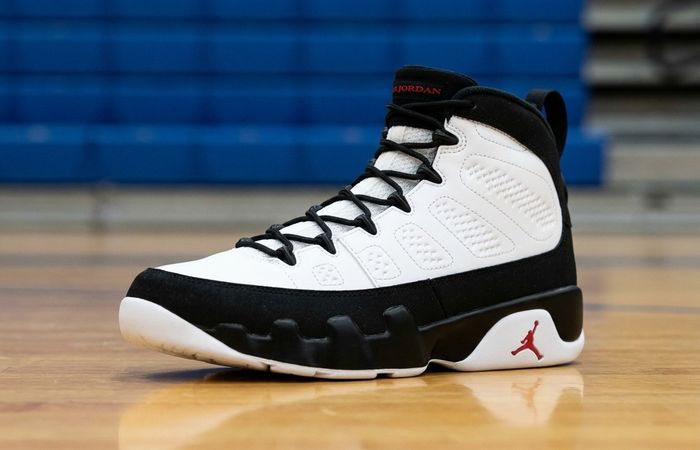 Air Jordan 9 Retro OG White and Black met rode details op een houten sporthalvloer