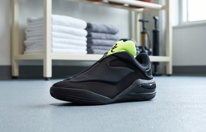 Converse SHAI 001 Shroud Shock met zwarte ritssluiting en geelgroene tong op een lichtblauwe vloer in een basketbalmateriaalruimte