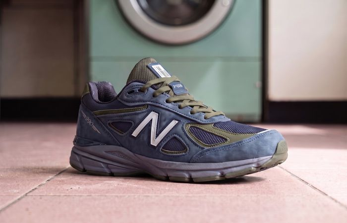 New Balance 990v4 Navy/Meteorite met blauwe nubuck, olijfgroene details en zilveren N op roze tegels in een wasserette