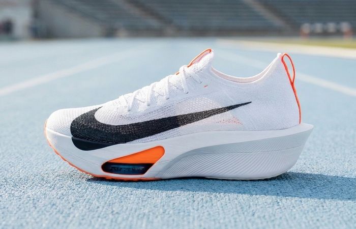 Nike Alphafly 4 in wit, zwart en oranje op een lichte hardloopbaan