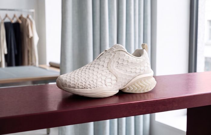 Puma x J.L-A.L CELL Geo Warm White met fijne TPU-kooi en open hielfins op een bordeauxrode plank in een atelier