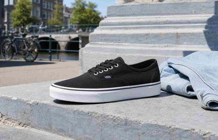 Zwarte Vans Authentic van canvas op een stenen stoep aan een zomerse stadsgracht